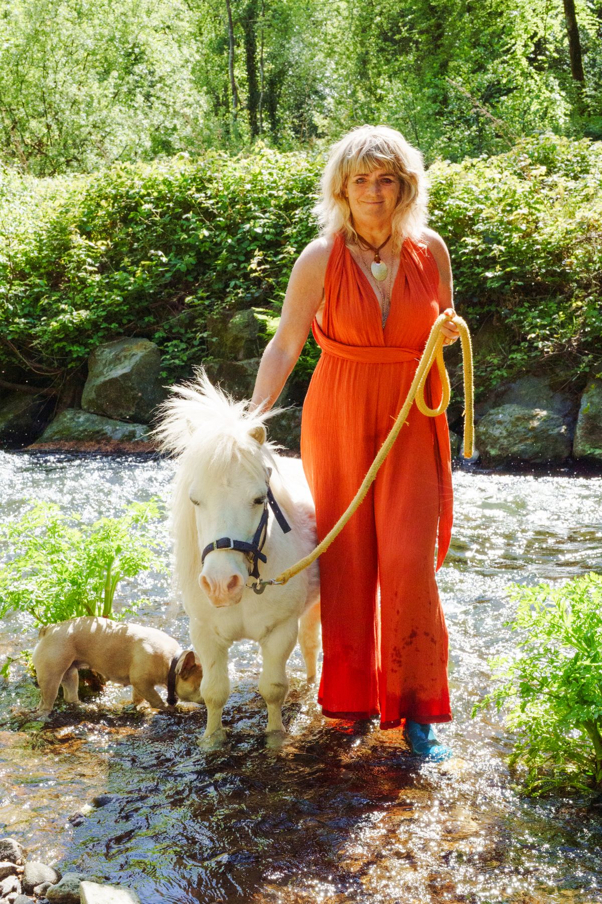 Carolyn leading a white pony through shallow river water