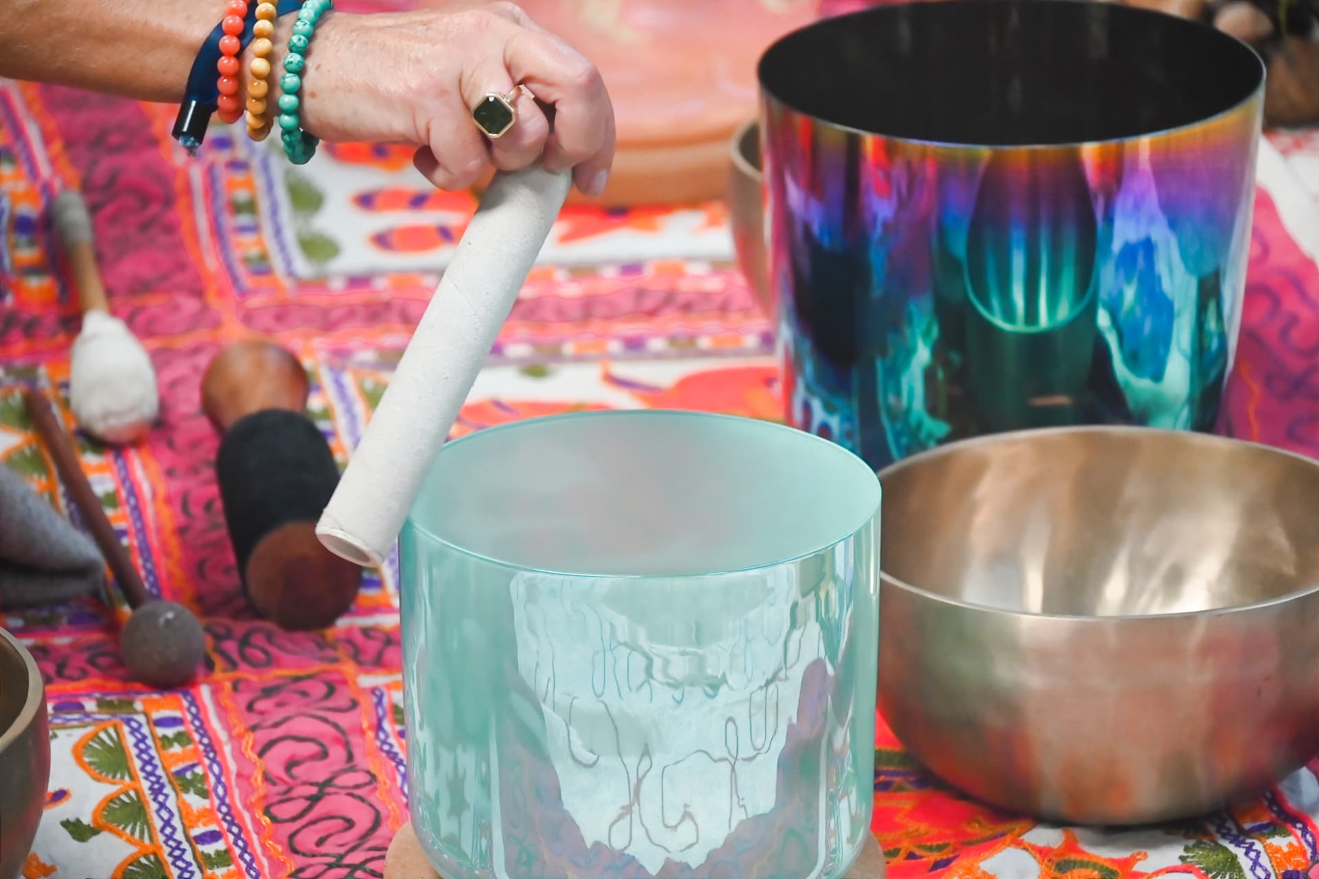 Hands sounding a crystal singing bowl on a bright embroidered cloth