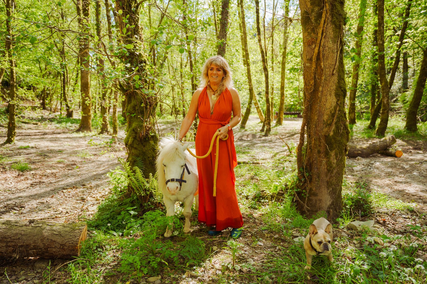 Carolyn standing with a small white pony beneath a mature tree
