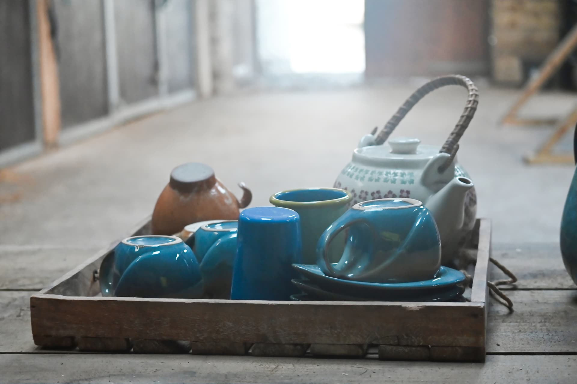 A wooden tray of blue cups and a teapot resting on the barn floor